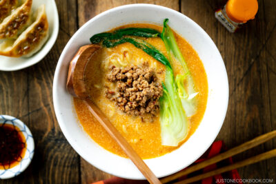 A white bowl containing Tan Tan Ramen (Tantanmen) which consists of ramen noodles and spicy creamy sesame soup, topped with savory ground pork mixture and blanched bok choy.