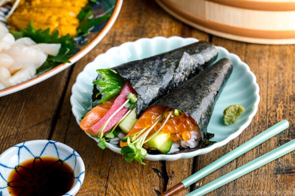 A light green plate containing two types of Temaki Sushi (Hand Roll Sushi) - salmon and tuna roll and salmon and ikura roll.