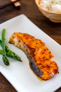 A white plate containing teriyaki salmon with glaze and asparagus.