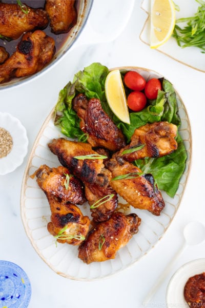 Teriyaki wings served on a white plate garnished with lemon, tomatoes and green lettuce.