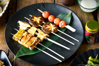 A ceramic plate containing Yakitori Style Grilled Vegetables along with Nigori Sake.