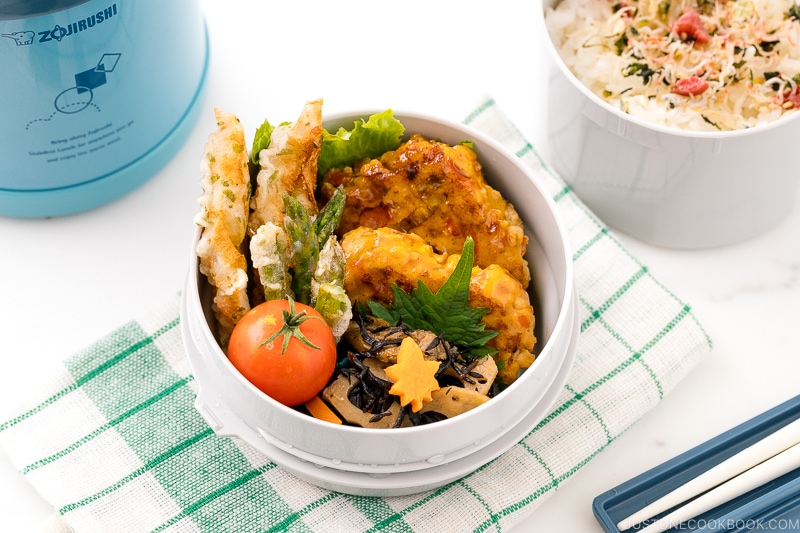 A Zojirushi lunch jar containing steamed rice, chicken meatballs, asparagus tempura, and hijiki salad.