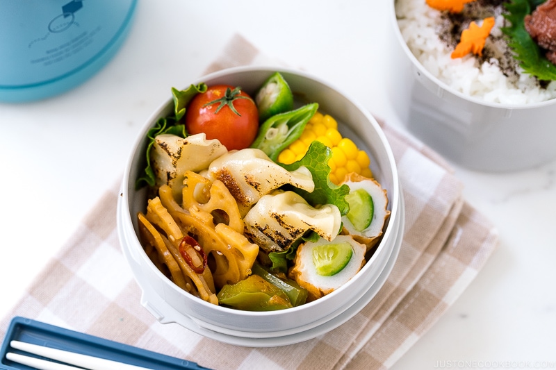 A Zojirushi lunch jar containing steamed rice, gyoza, and chikuwa cucumber.